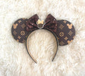 Handcrafted Heritage Luxe Boutique mouse ear headband featuring a rich brown designer-inspired print with subtle mouse silhouettes, an espresso sequin bow, pearl trim, decorative mouse silhouette centerpiece, and a lightweight comfort-fit headband.
