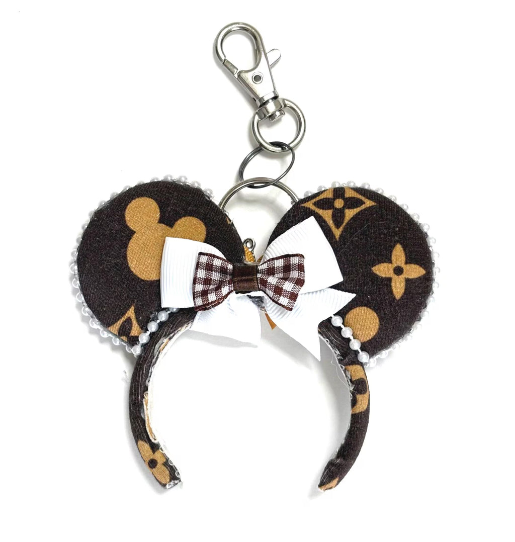 Heritage Luxe Mini handcrafted mouse ear bag charm featuring an espresso and gold heritage-inspired print, satin gold bow, pearl trim, and coordinating design with the Heritage Luxe headband.