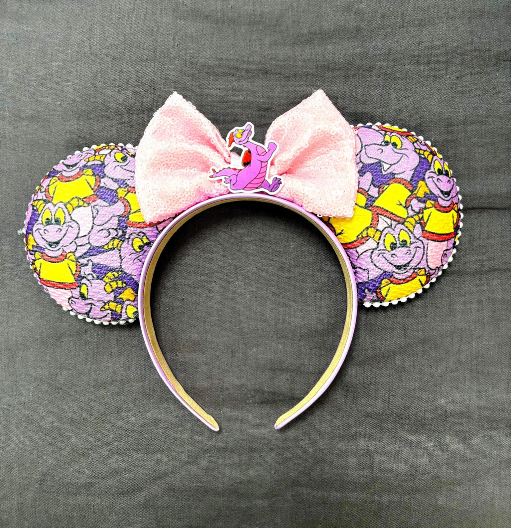 Imagination Journey Boutique Mouse Ear Headband from the Pixie Park Essentials Collection featuring whimsical purple dragon-inspired artwork, a soft pink bow, handcrafted lightweight construction, and comfortable all-day wear.