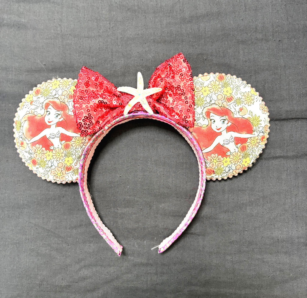 Mermaid Shores boutique mouse ear headband featuring ocean-inspired princess artwork, red sequin bow, starfish centerpiece, and pearl trim.