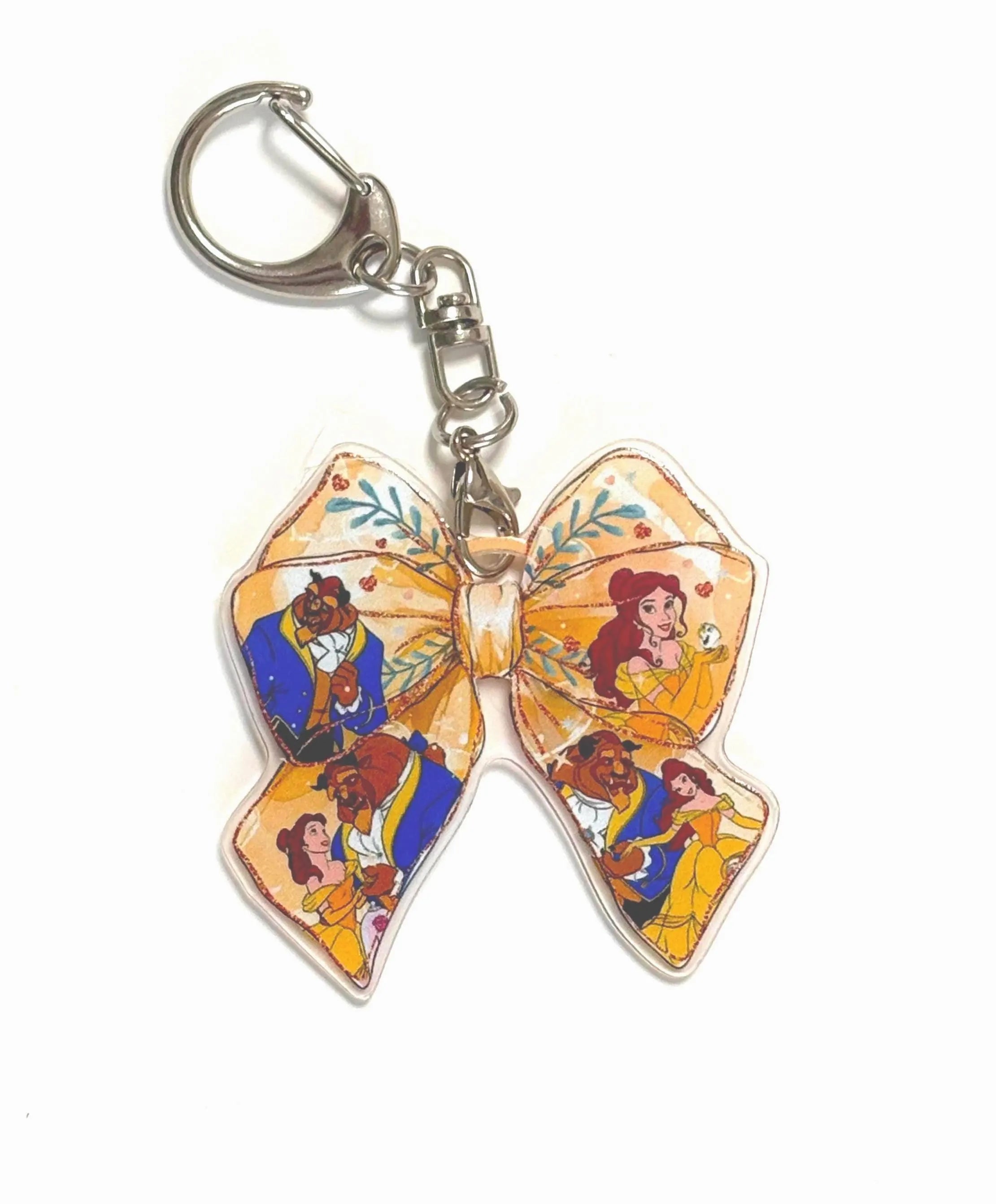 Belle's Bow Pocket Charm featuring a ribbon-shaped resin charm with fairy tale-inspired artwork in warm golden tones, attached to a silver lobster clasp and key ring.