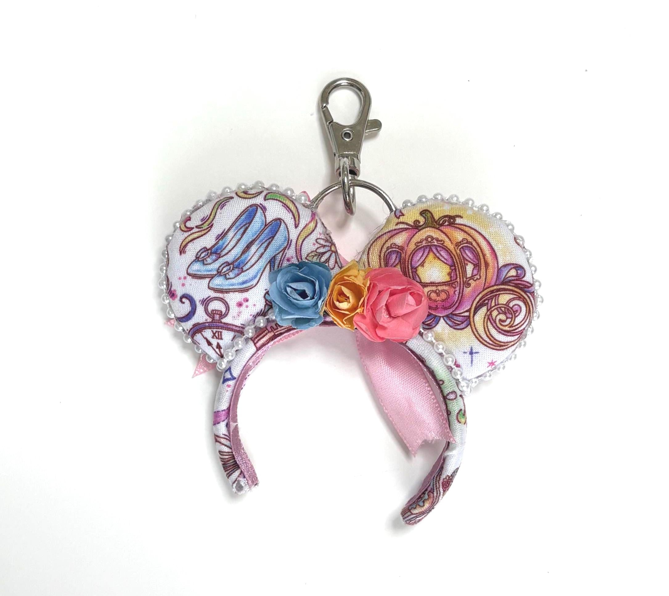 Palace Dreams Mini handcrafted mouse ear bag charm featuring a fairytale-inspired castle, carriage, glass slipper print, floral centerpiece, satin ribbon accents, and pearl trim.