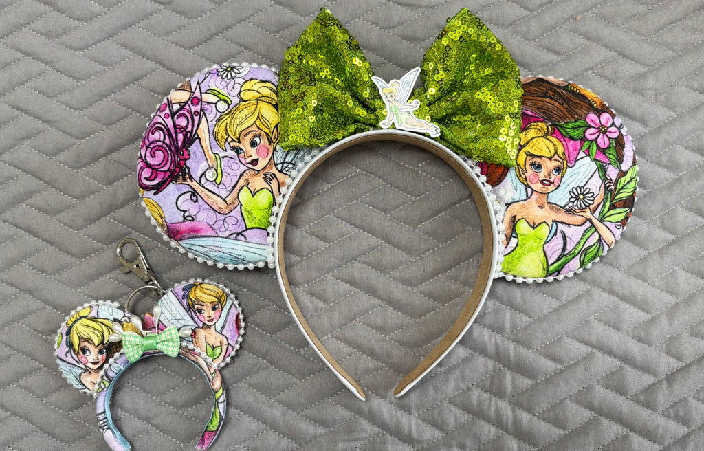 Handcrafted Pixie Dust Pixie Pair featuring a fairy-inspired mouse ear headband and coordinating Mini Magic Charm with pastel fairy artwork, shimmering green sequin bow, decorative pearl trim, and handcrafted boutique styling.