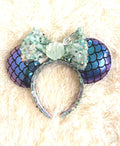 Handcrafted ocean-inspired boutique mouse ear headband featuring shimmering fish-scale patterned ears, a sparkling seafoam sequined bow, and a seashell centerpiece from Pixie Park Co.

Tags