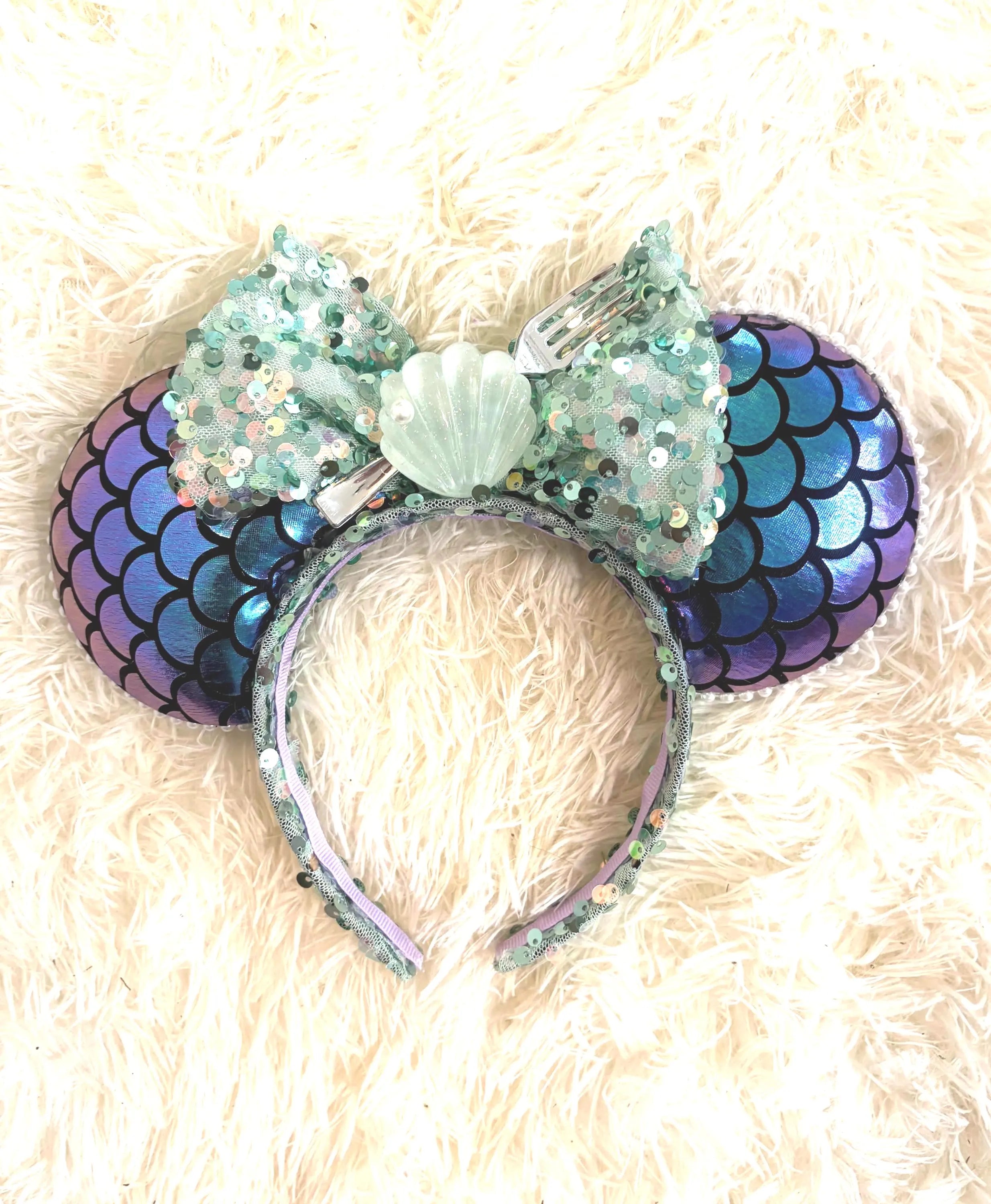 Handcrafted ocean-inspired boutique mouse ear headband featuring shimmering fish-scale patterned ears, a sparkling seafoam sequined bow, and a seashell centerpiece from Pixie Park Co.

Tags