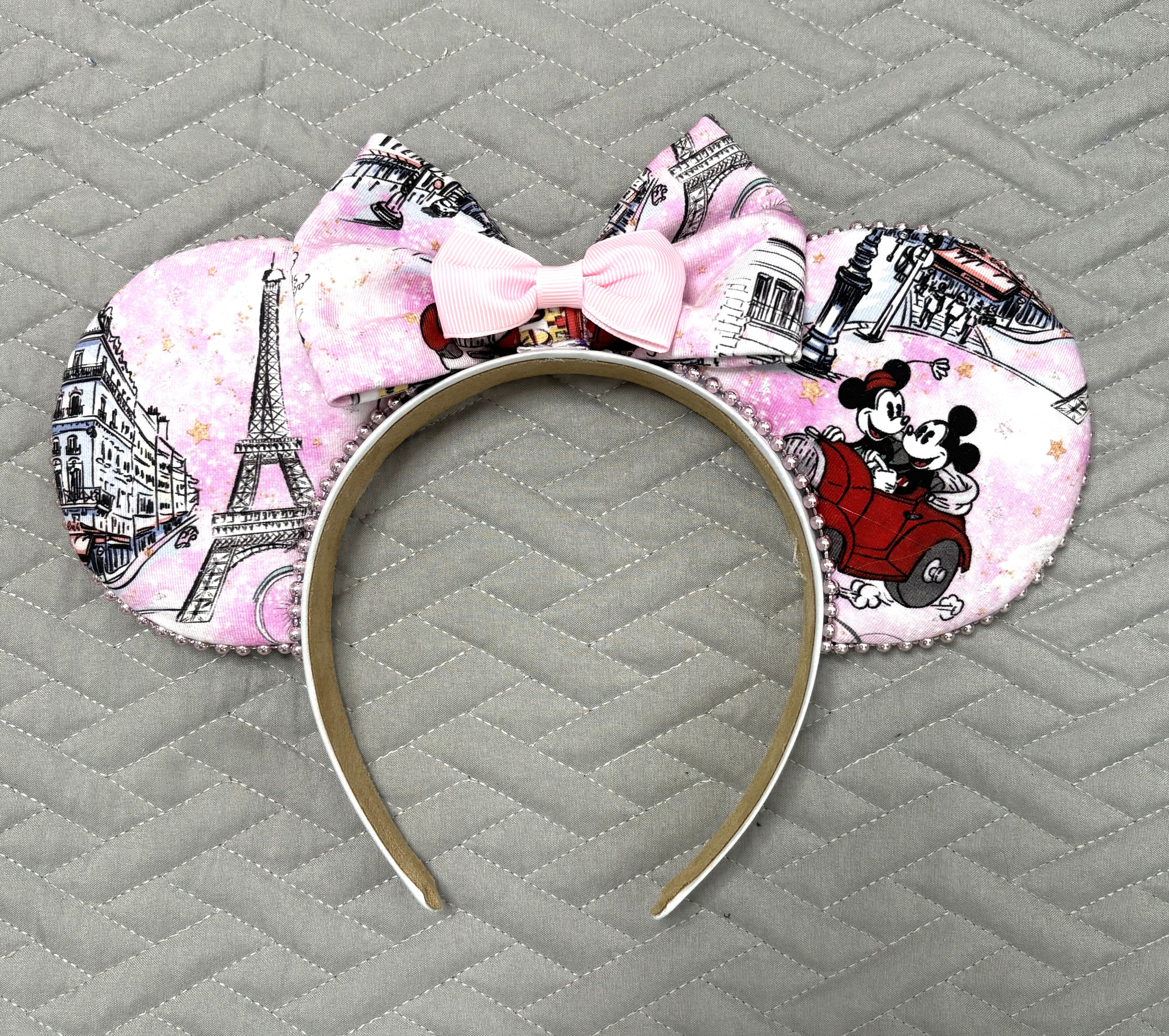 Handcrafted Bonjour Paris mouse ear headband featuring Paris-inspired artwork with iconic European landmarks, pearl trim, and a soft blush bow.