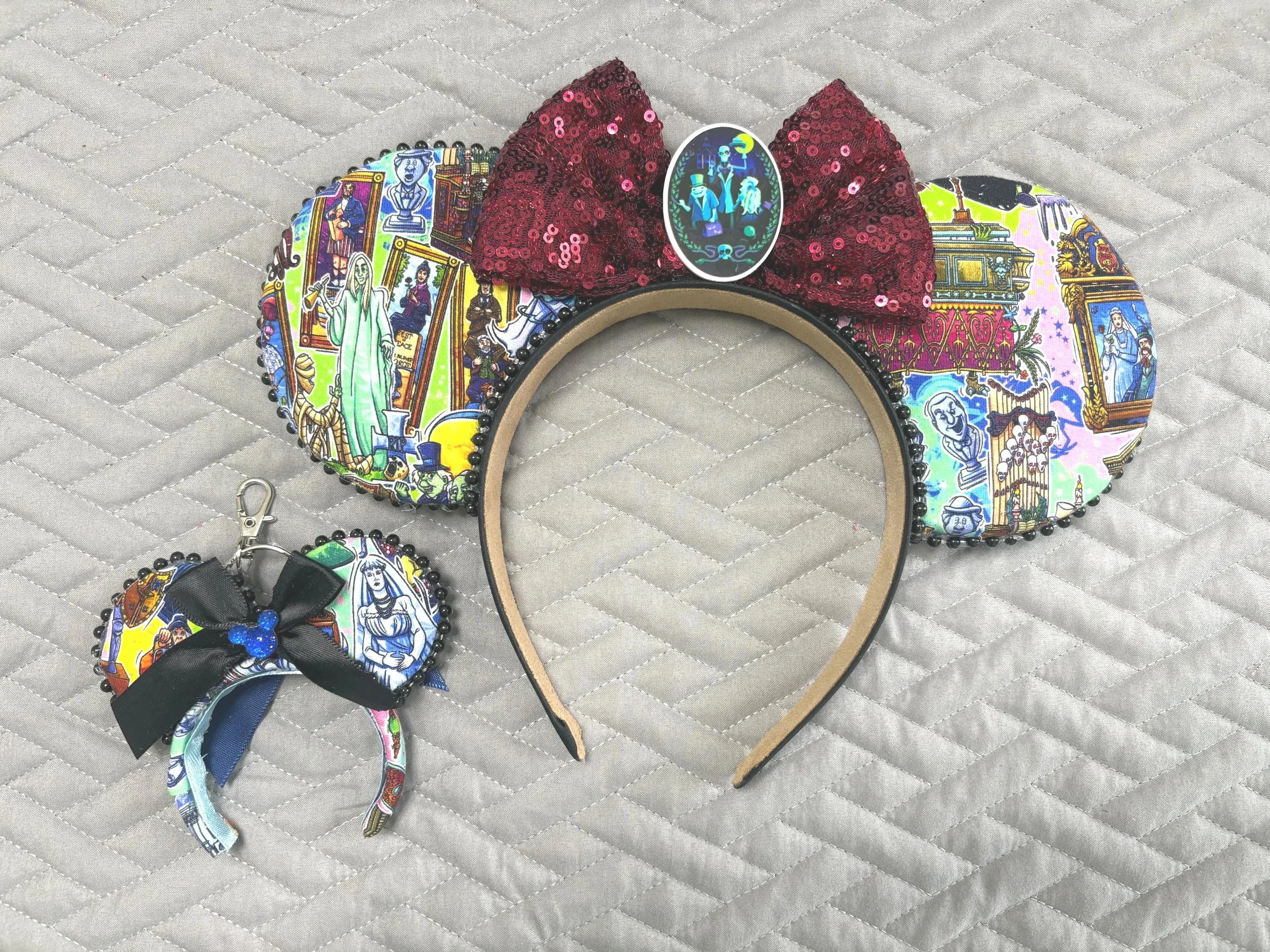 Handcrafted Haunted Manor Pixie Pair featuring a haunted attraction-inspired mouse ear headband and coordinating Mini Magic Charm with ghostly portraits, gothic manor artwork, burgundy sequin bow, black beaded trim, and handcrafted boutique styling.