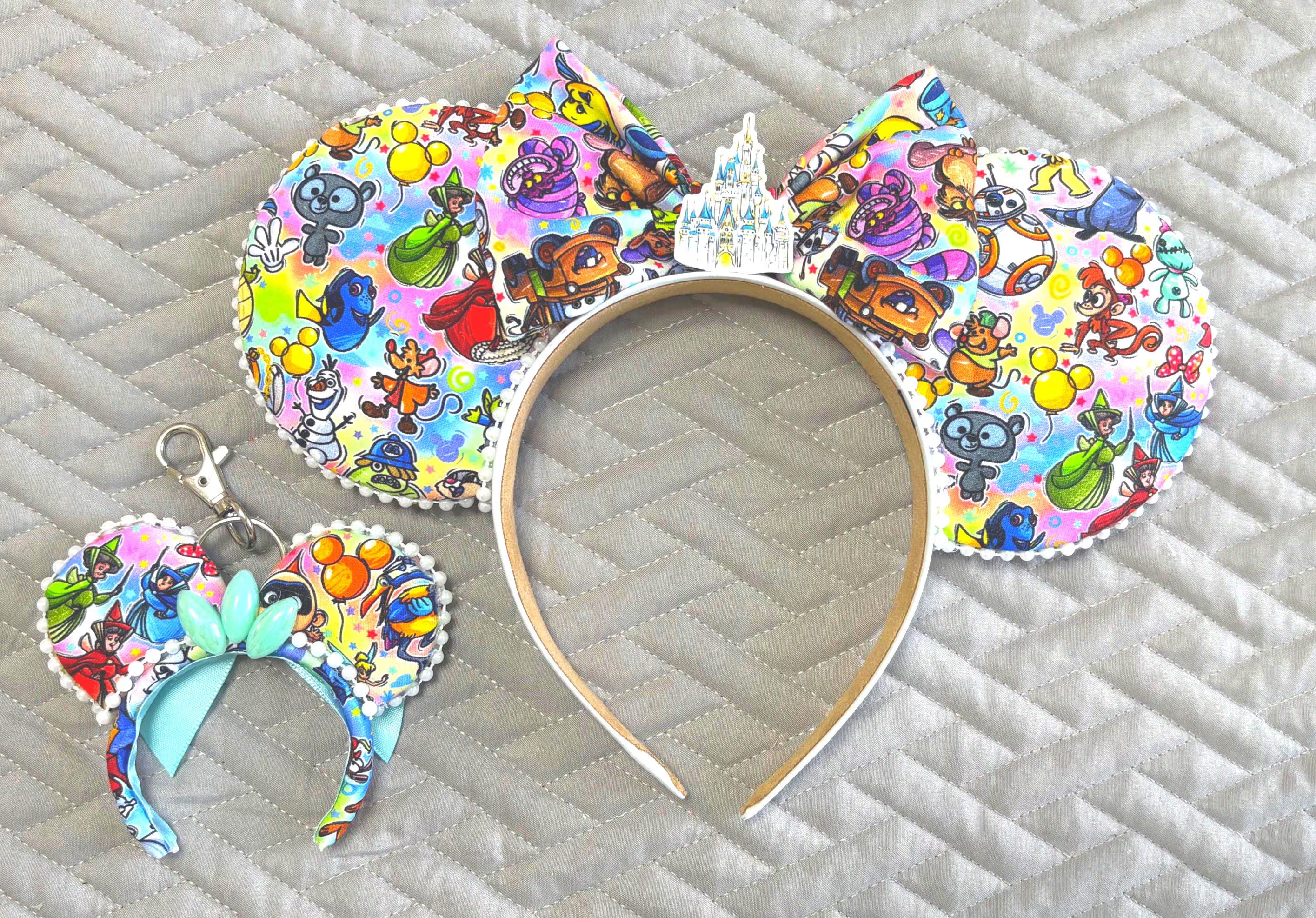 Handcrafted Park Celebration Pixie Pair featuring a matching mouse ear headband and coordinating Mini Magic Charm with colorful park-inspired artwork, classic attractions, favorite characters, decorative castle centerpiece, boutique bow, beaded trim, and handcrafted boutique styling.
