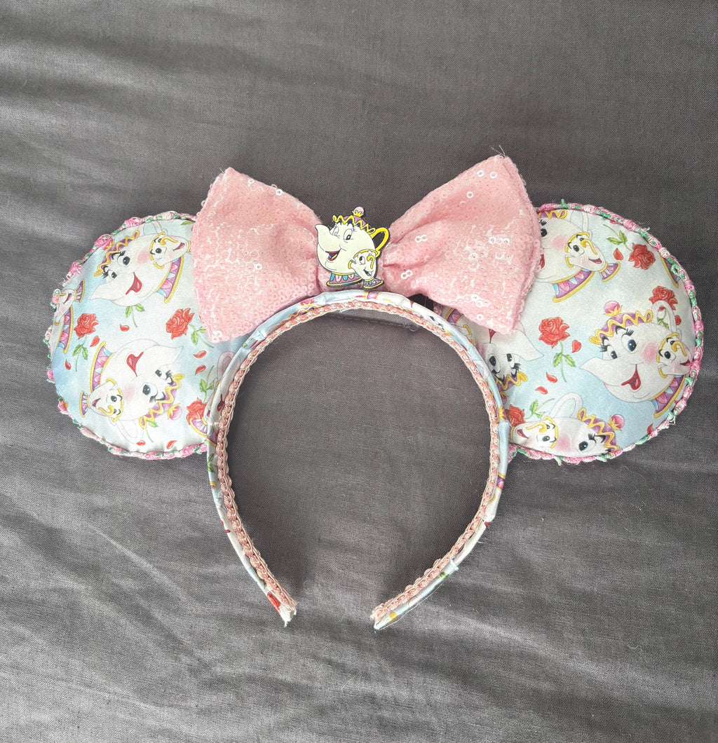 Enchanted Tea Party Boutique Mouse Ear Headband from the Pixie Park Essentials Collection featuring handcrafted mouse ears with teacup-inspired artwork, a soft pink sequin bow, decorative tea party centerpiece, and lightweight comfort-fit design.