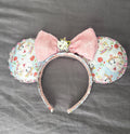 Enchanted Tea Party Boutique Mouse Ear Headband from the Pixie Park Essentials Collection featuring handcrafted mouse ears with teacup-inspired artwork, a soft pink sequin bow, decorative tea party centerpiece, and lightweight comfort-fit design.