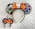 Handcrafted Spooky Park Bones Pixie Pair featuring a matching mouse ear headband and coordinating Mini Magic Charm with colorful skeleton-inspired mouse artwork, bright orange sequined bows, decorative beaded trim, and festive Halloween boutique styling.