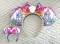 Handcrafted Castle Dreams Pixie Pair featuring a matching mouse ear headband and coordinating Mini Magic Charm with fairytale castle artwork, pink-to-gold ombré sequin bow, decorative beaded trim, and handcrafted boutique styling.
