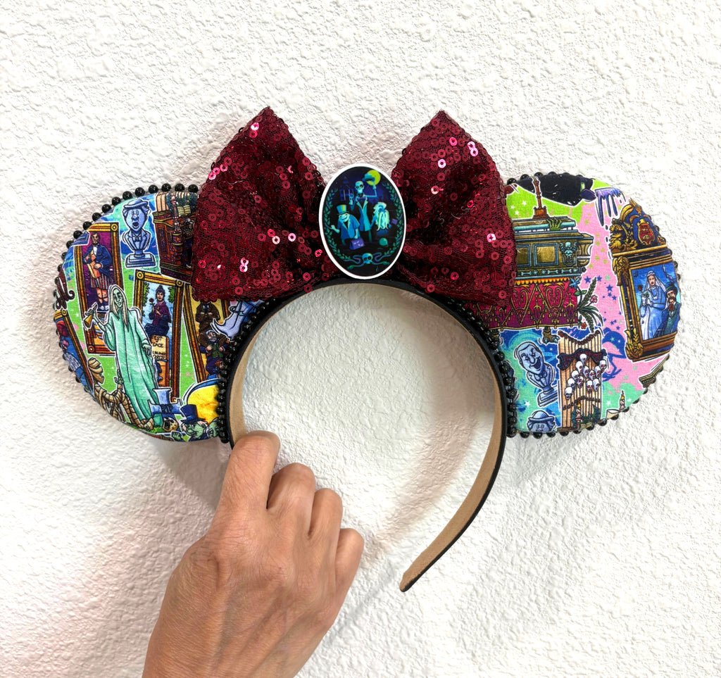 Handcrafted Haunted Manor mouse ear headband featuring haunted estate-inspired artwork, a burgundy sequin bow, and black beaded trim.