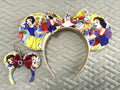 Handcrafted Enchanted Princess Pixie Pair featuring a princess-inspired mouse ear headband with elegant storybook artwork, pearl trim, coordinating princess centerpiece, and matching Mini Magic Charm with ruby-red boutique bow and sparkling jewel accent.