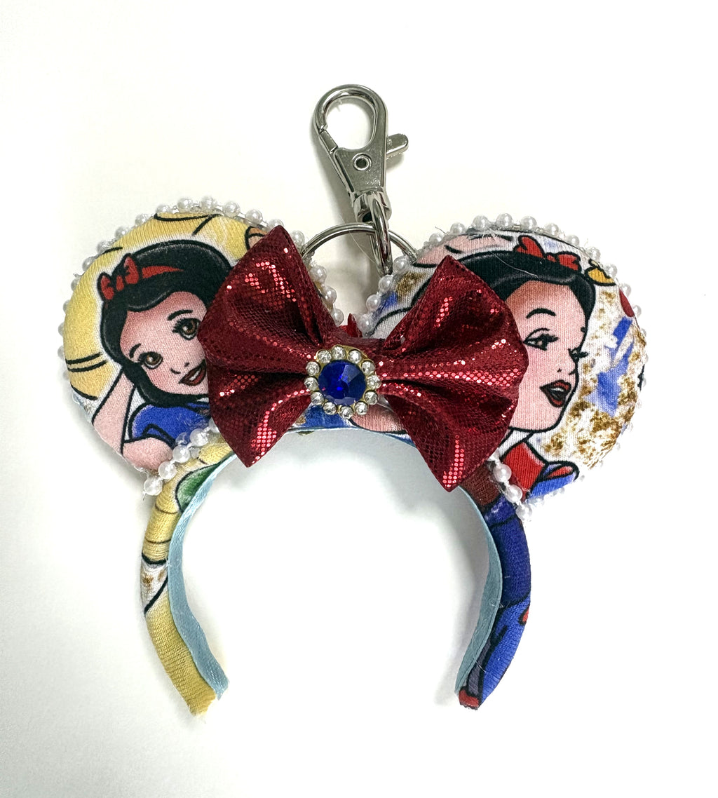 Handcrafted Enchanted Princess mini mouse ear bag charm featuring fairy tale-inspired artwork, a ruby-red jeweled bow with sparkling gem, decorative beaded trim, and boutique handcrafted styling.