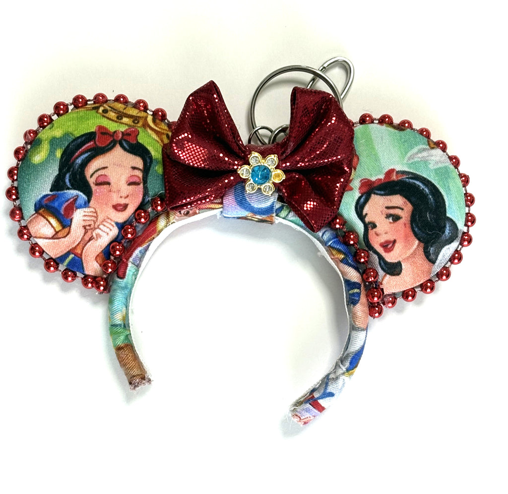Handcrafted Magic Mirror mini mouse ear bag charm featuring fairy tale-inspired princess artwork, ruby-red sequined bow with jeweled center, decorative beaded trim, and boutique handcrafted styling for bags and keychains.