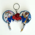 Handcrafted Storybook Belle mini mouse ear bag charm featuring fairy tale-inspired artwork, sparkling sapphire-blue bow with handcrafted rose accents, decorative beaded trim, and boutique handcrafted styling for handbags, backpacks, and keychains.