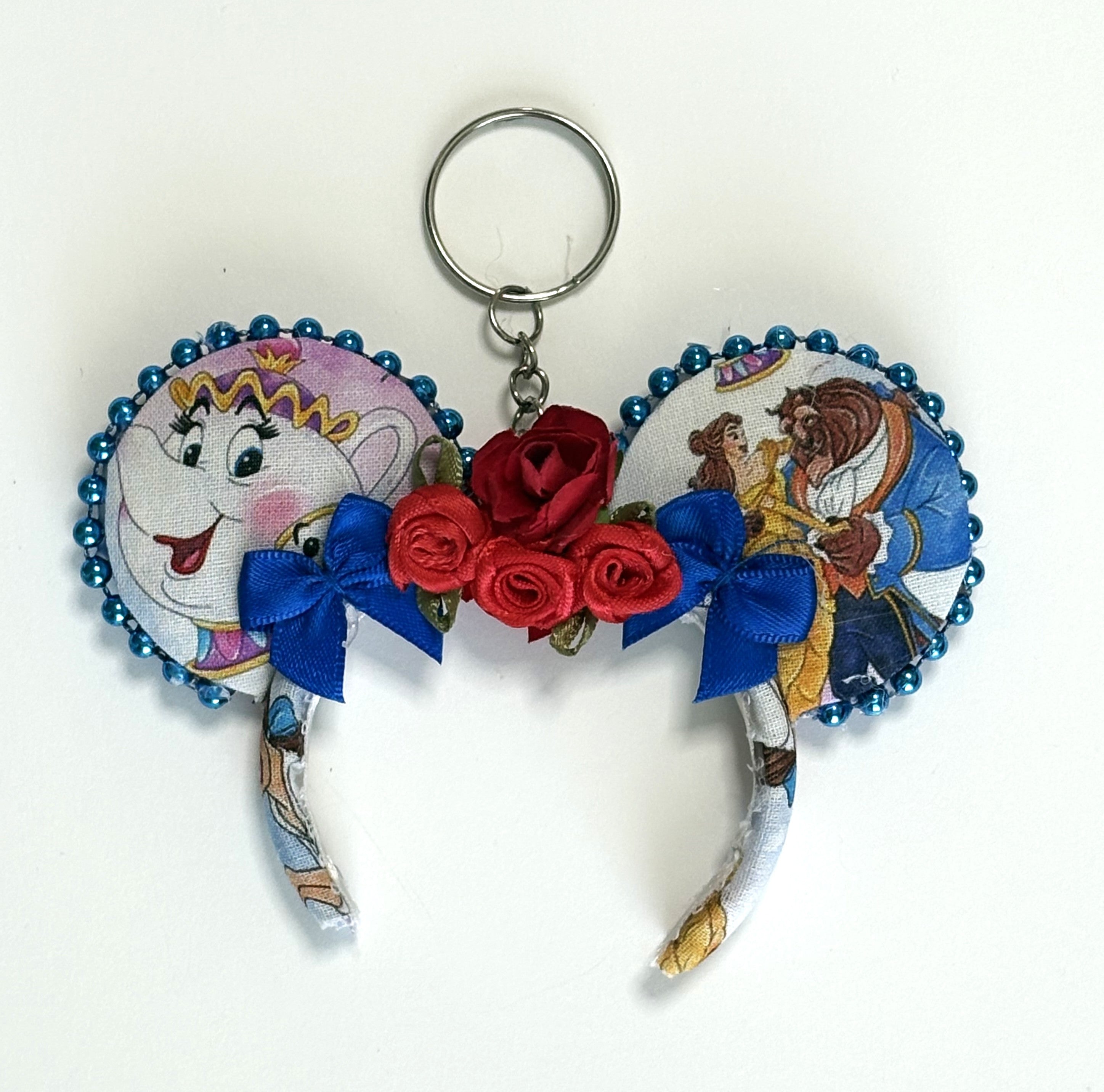 Handcrafted Storybook Belle mini mouse ear bag charm featuring fairy tale-inspired artwork, sparkling sapphire-blue bow with handcrafted rose accents, decorative beaded trim, and boutique handcrafted styling for handbags, backpacks, and keychains.