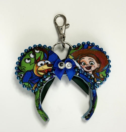 Handcrafted Cosmic Claw mini mouse ear bag charm featuring playful space adventure-inspired artwork, an emerald-green sequined bow with an alien-themed centerpiece, decorative beaded trim, and boutique handcrafted styling for handbags, backpacks, luggage, and keychains.