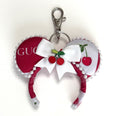 Handcrafted Cherry Belle mini mouse ear bag charm featuring cherry-inspired boutique artwork, decorative pearl trim, a layered red satin bow with floral center embellishment, and a lobster clasp for attaching to handbags, backpacks, luggage, or keychains.
