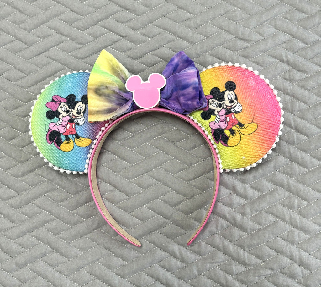Handcrafted rainbow-inspired mouse ear headband featuring colorful pastel artwork, a hand-tied watercolor bow, and boutique handcrafted styling.