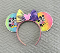 Handcrafted rainbow-inspired mouse ear headband featuring colorful pastel artwork, a hand-tied watercolor bow, and boutique handcrafted styling.