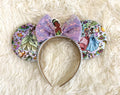 Handcrafted bayou-inspired mouse ear headband featuring blooming floral artwork, soft lavender tones, an iridescent sequin bow, and elegant boutique styling.