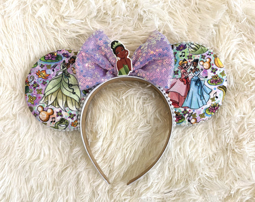 Handcrafted bayou-inspired mouse ear headband featuring blooming floral artwork, soft lavender tones, an iridescent sequin bow, and elegant boutique styling.