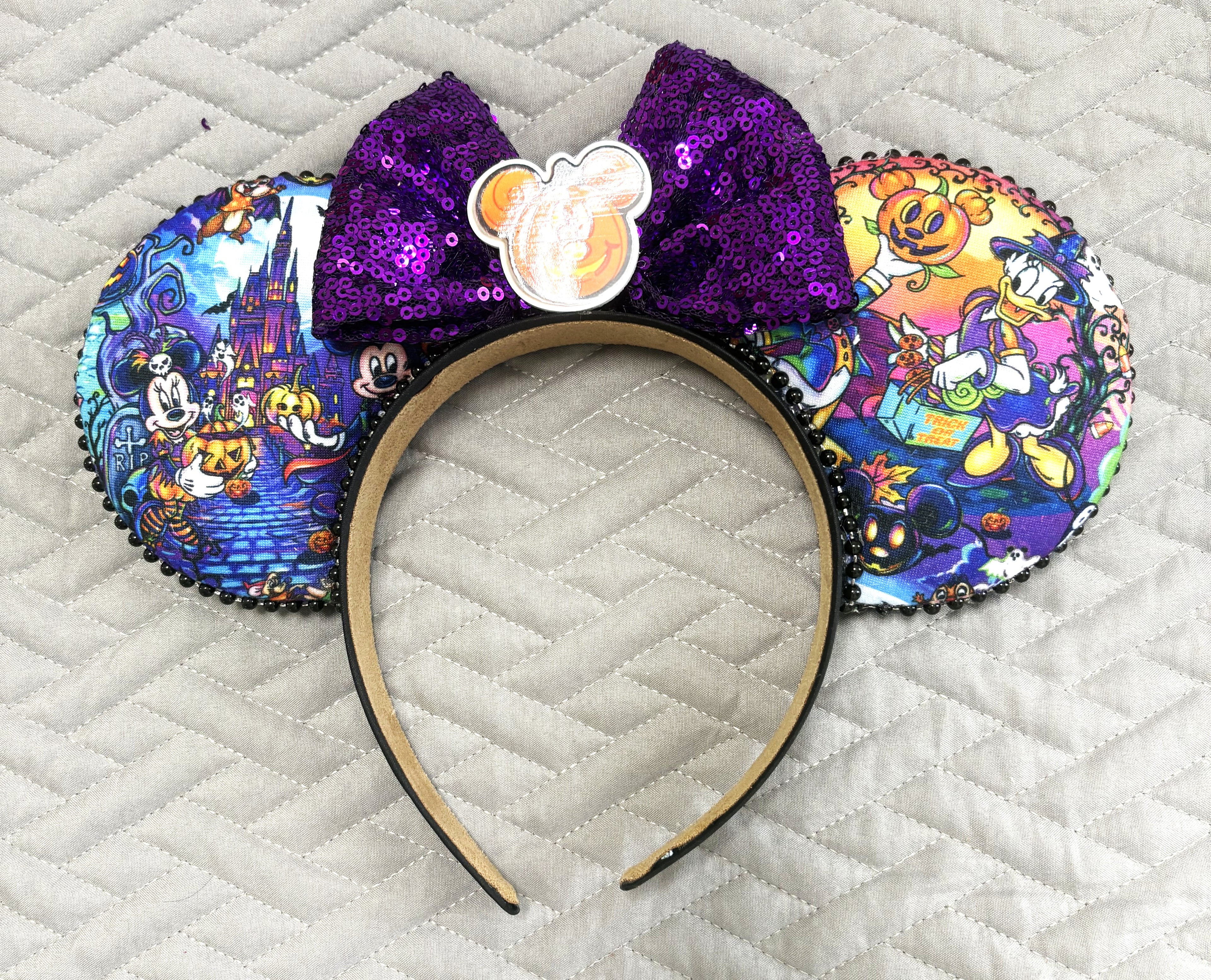 Handcrafted Pumpkin Parade Signature mouse ear headband featuring colorful Halloween-inspired artwork, a sparkling purple sequined bow, a pumpkin centerpiece, decorative trim, and boutique craftsmanship by Pixie Park Company.