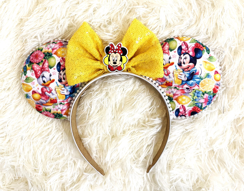 Handcrafted Lemon Blossom Signature mouse ear headband featuring colorful citrus-inspired artwork, a sparkling yellow sequined bow, decorative pearl trim, and boutique craftsmanship by Pixie Park Company.