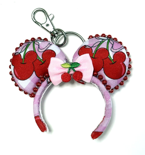 Handcrafted Cherry Jubilee Mini Magic Charm featuring cherry-inspired artwork, a pink boutique bow with sparkling accents, a miniature mouse ear design, and a lobster clasp by Pixie Park Company.