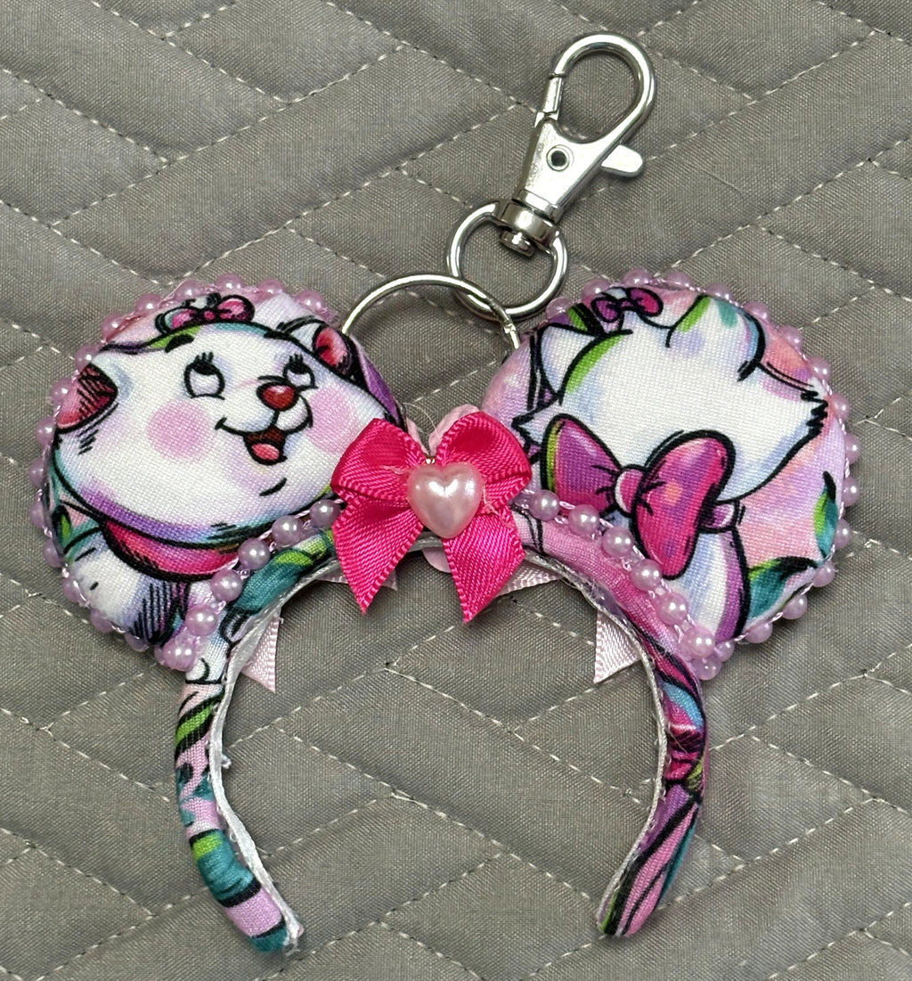 Pixie Park Company Couture Cats Mini Magic Charm featuring Paris-inspired pastel kitten artwork, a shimmering lavender boutique bow, decorative white beaded trim, and a coordinating keyring attachment.