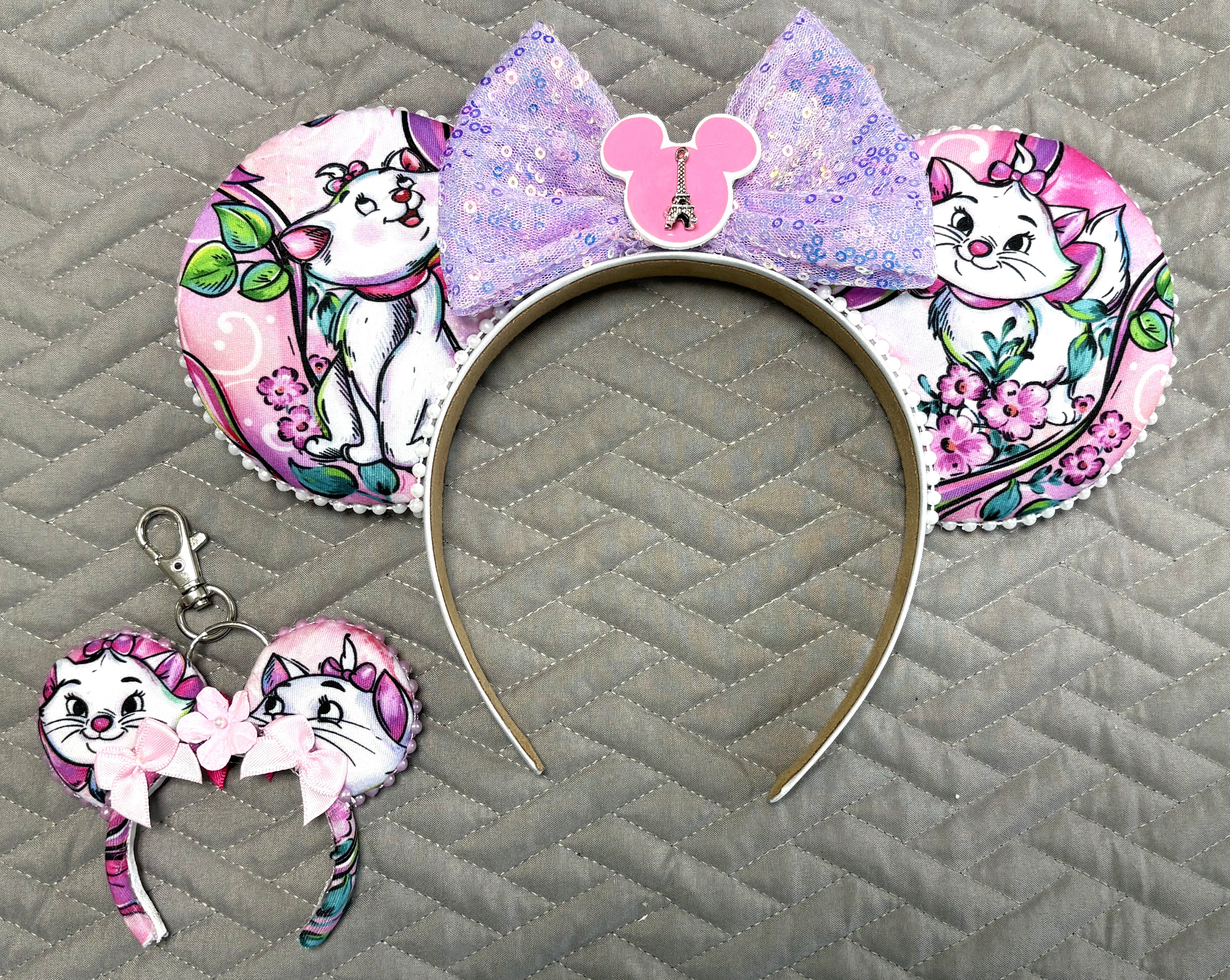 Pixie Park Company Couture Cats Pixie Pair featuring a coordinated Signature mouse ear headband and matching Mini Magic Charm with Paris-inspired pastel kitten artwork, a shimmering lavender sequin bow, decorative white beaded trim, and handcrafted boutique styling.
