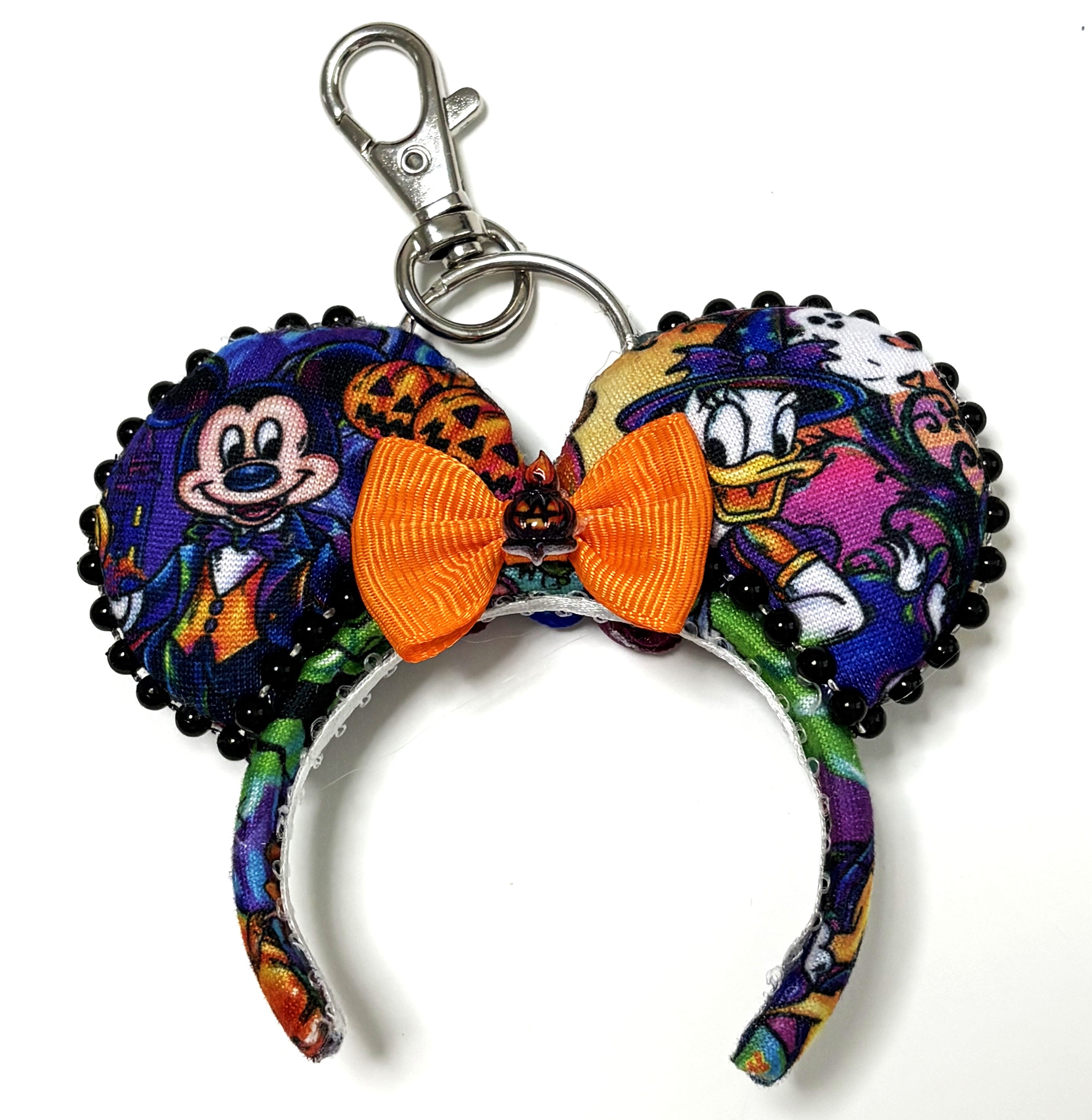 Pixie Park Company Pumpkin Parade Mini Magic Charm featuring festive Halloween-inspired artwork, a bright orange boutique bow, decorative black beaded trim, a miniature jack-o'-lantern centerpiece, and a silver keyring with lobster clasp attachment.