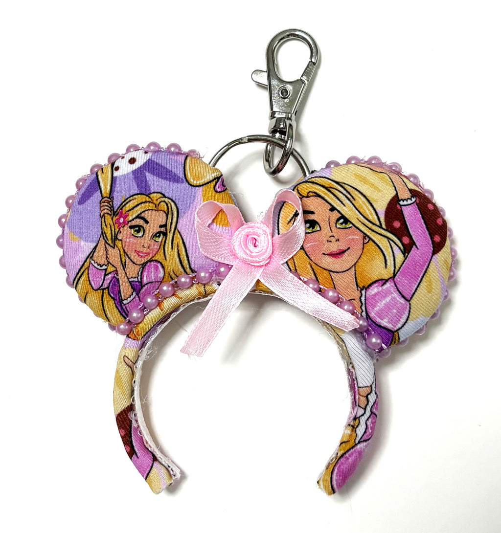 Pixie Park Company Golden Dreams Mini Magic Charm featuring elegant golden-inspired artwork, a coordinating boutique bow, decorative beaded trim, and a silver keyring with lobster clasp attachment.