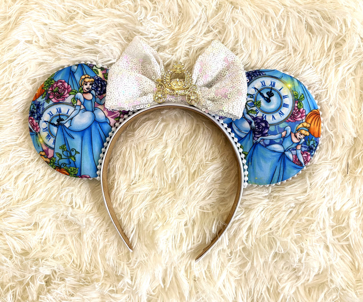 Midnight Carriage handcrafted princess-inspired mouse ear headband with blue fairy-tale fabric, clock and pumpkin details, white iridescent sequin bow, pearl trim and gold carriage centerpiece.