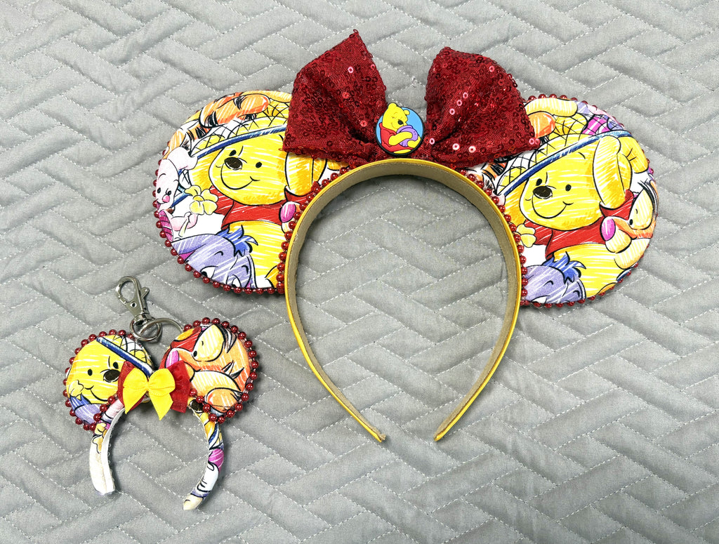 Honey Bear & Friends Pixie Pair featuring a handcrafted mouse ear headband and matching Mini Magic Charm with colorful honey-bear and woodland-friend imagery, red accents and decorative trim.