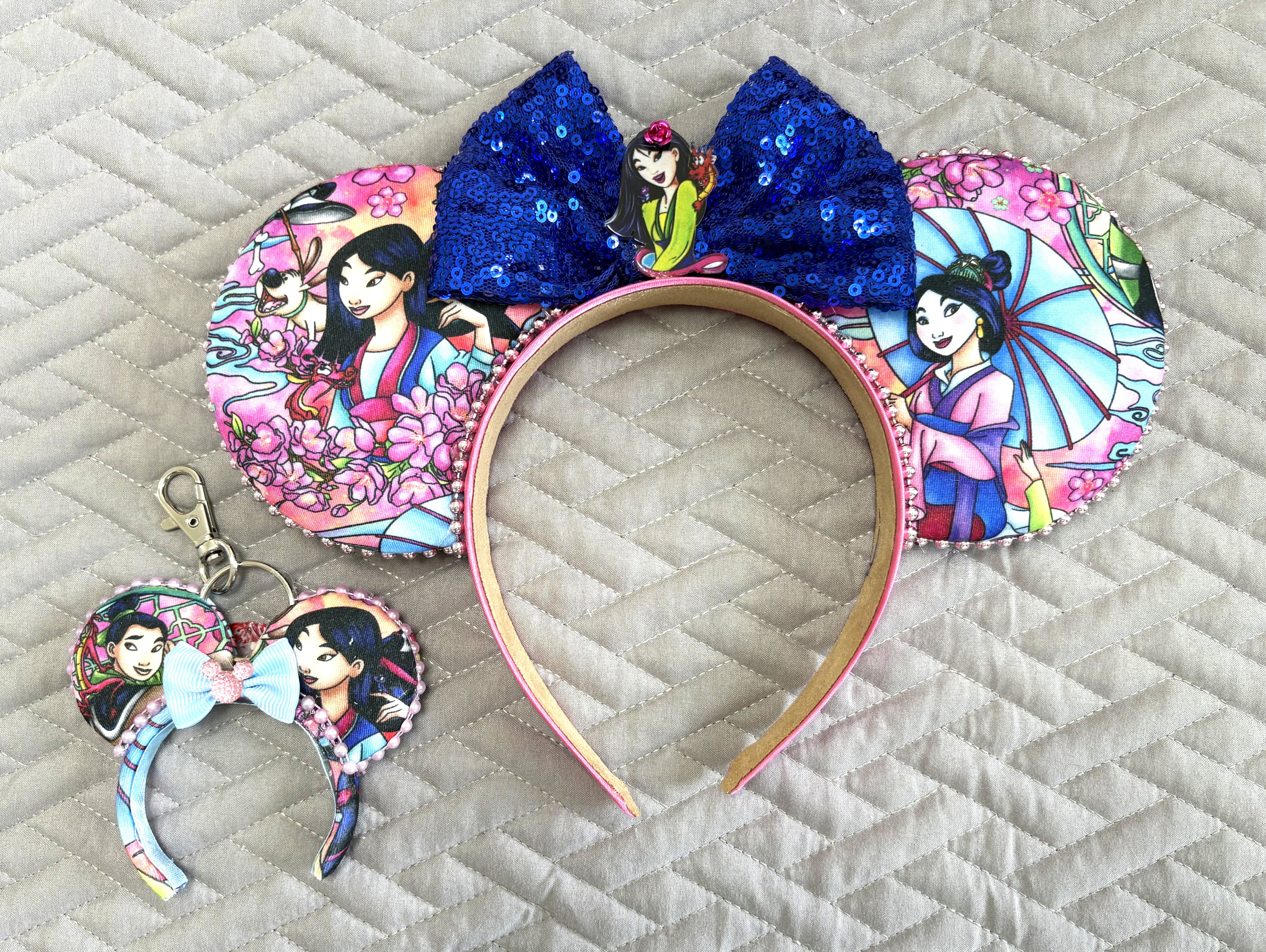 Blossom Warrior handcrafted mini ear charm featuring heroine-inspired imagery, pink blossom details, rich blue accents, coordinating bow, lobster clasp and split ring.