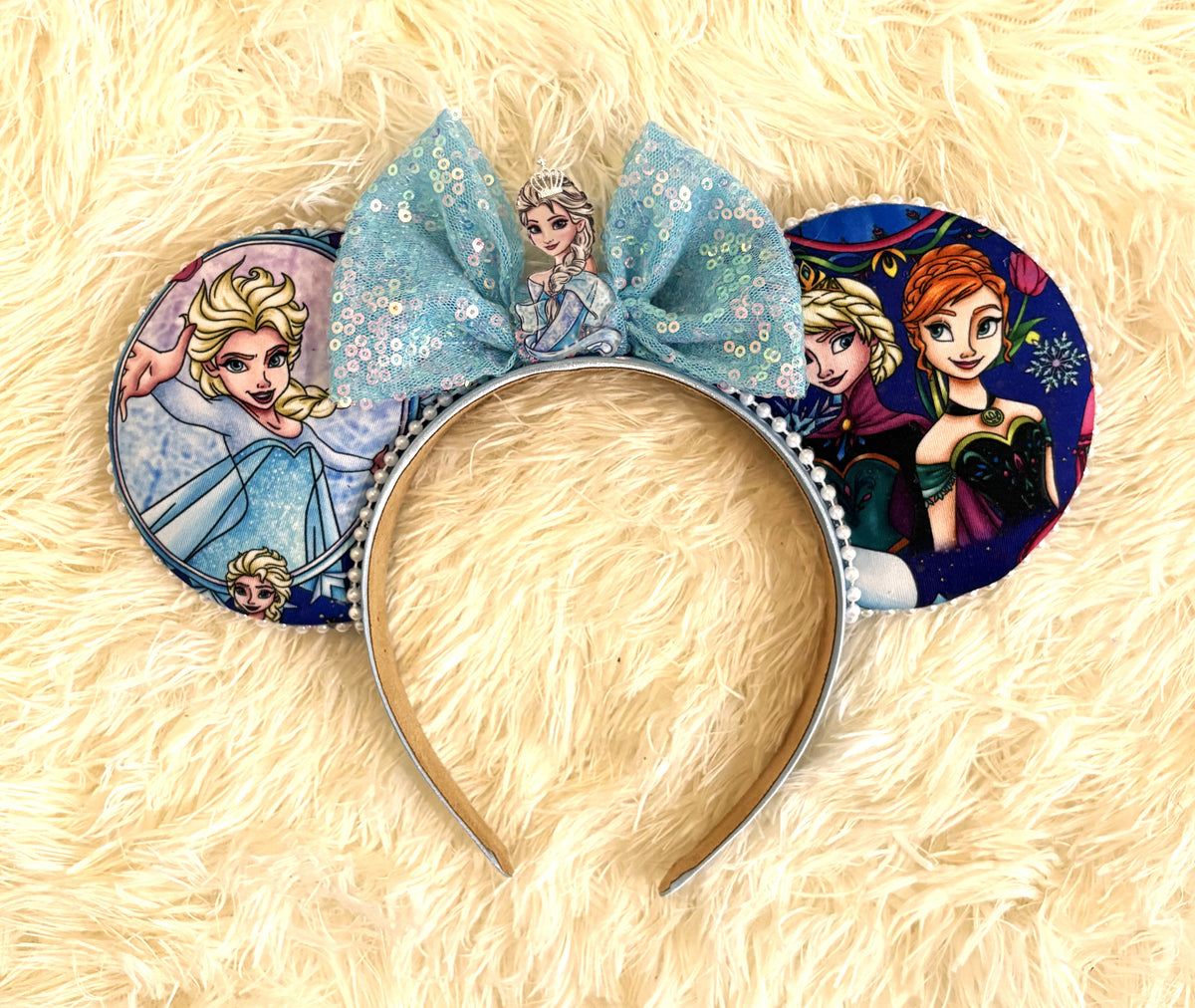Sisters of Winter handcrafted mouse ear headband featuring two winter-princess-inspired sisters, icy blue storybook imagery, sparkling blue sequin bow and white beaded trim.