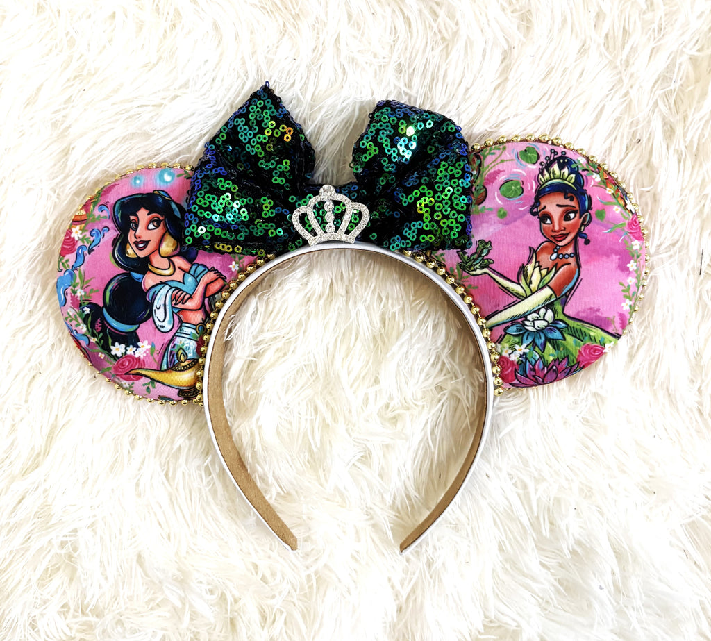 Handcrafted Emerald Wishes Princess Duo mouse ear headband featuring two princess-inspired designs, an emerald and teal sequined bow, jeweled crown centerpiece, pink floral fabric, and gold beaded trim by Pixie Park Co.