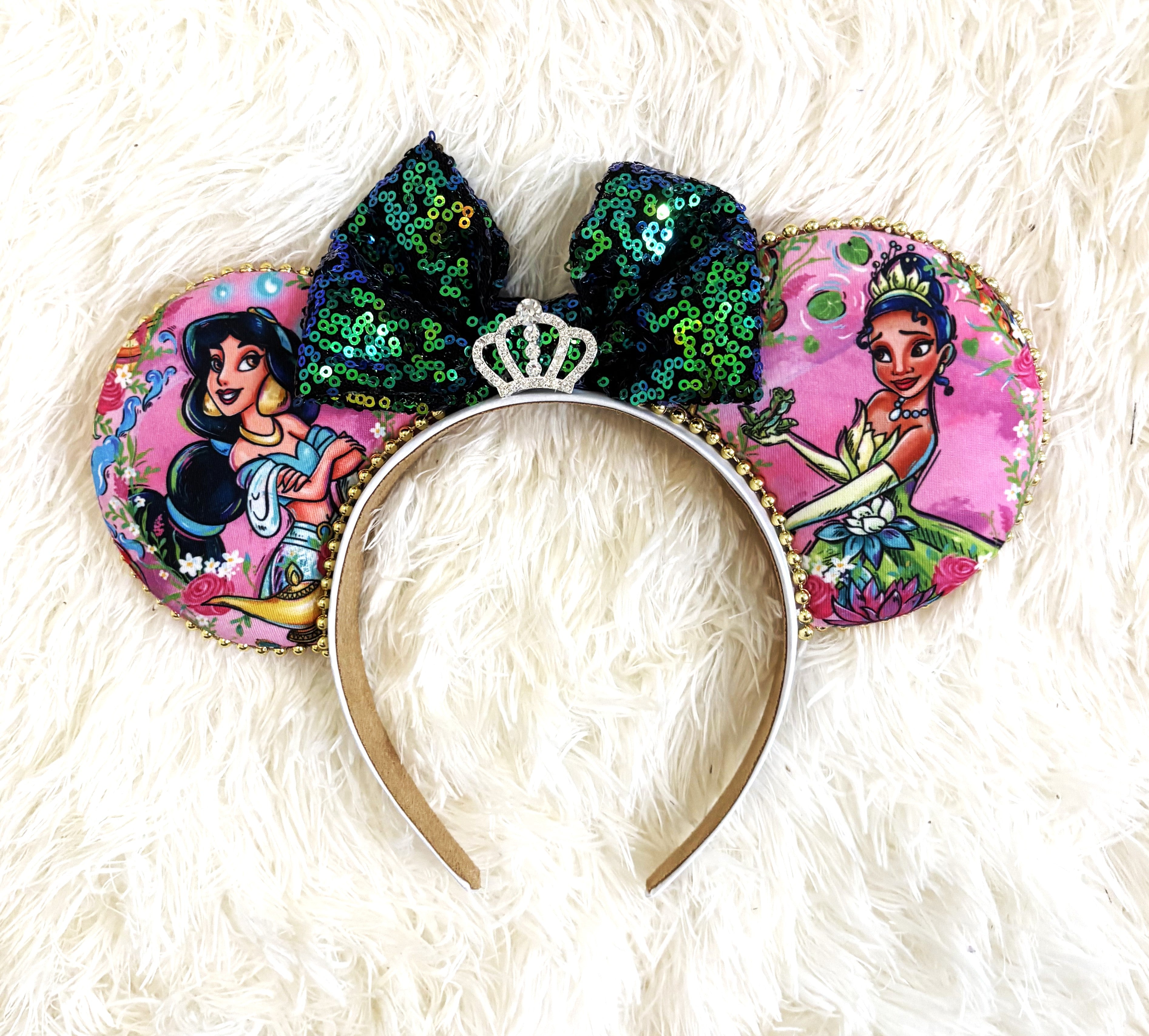Handcrafted Emerald Wishes Princess Duo mouse ear headband featuring two princess-inspired designs, an emerald and teal sequined bow, jeweled crown centerpiece, pink floral fabric, and gold beaded trim by Pixie Park Co.