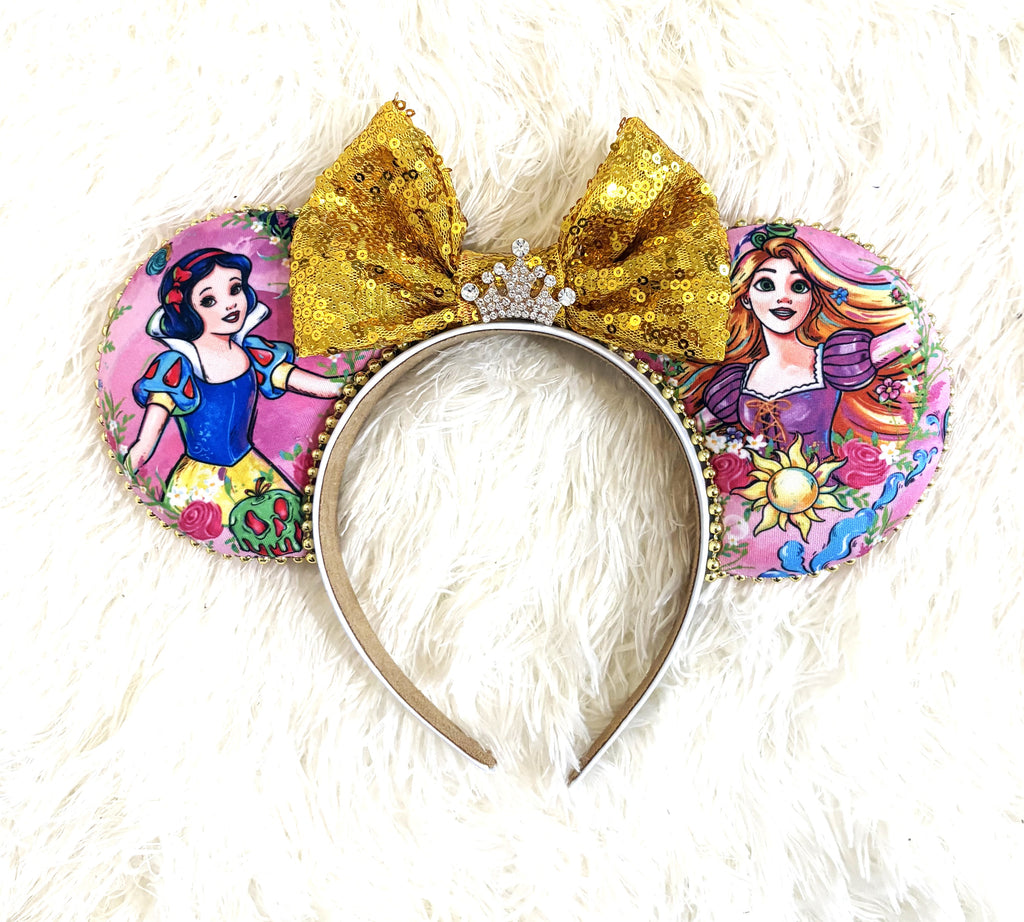 Handcrafted Golden Reflection Princess Duo mouse ear headband featuring two fairy-tale princess-inspired designs, a gold sequined bow, jeweled crown centerpiece, pink floral fabric, and gold beaded trim by Pixie Park Co.