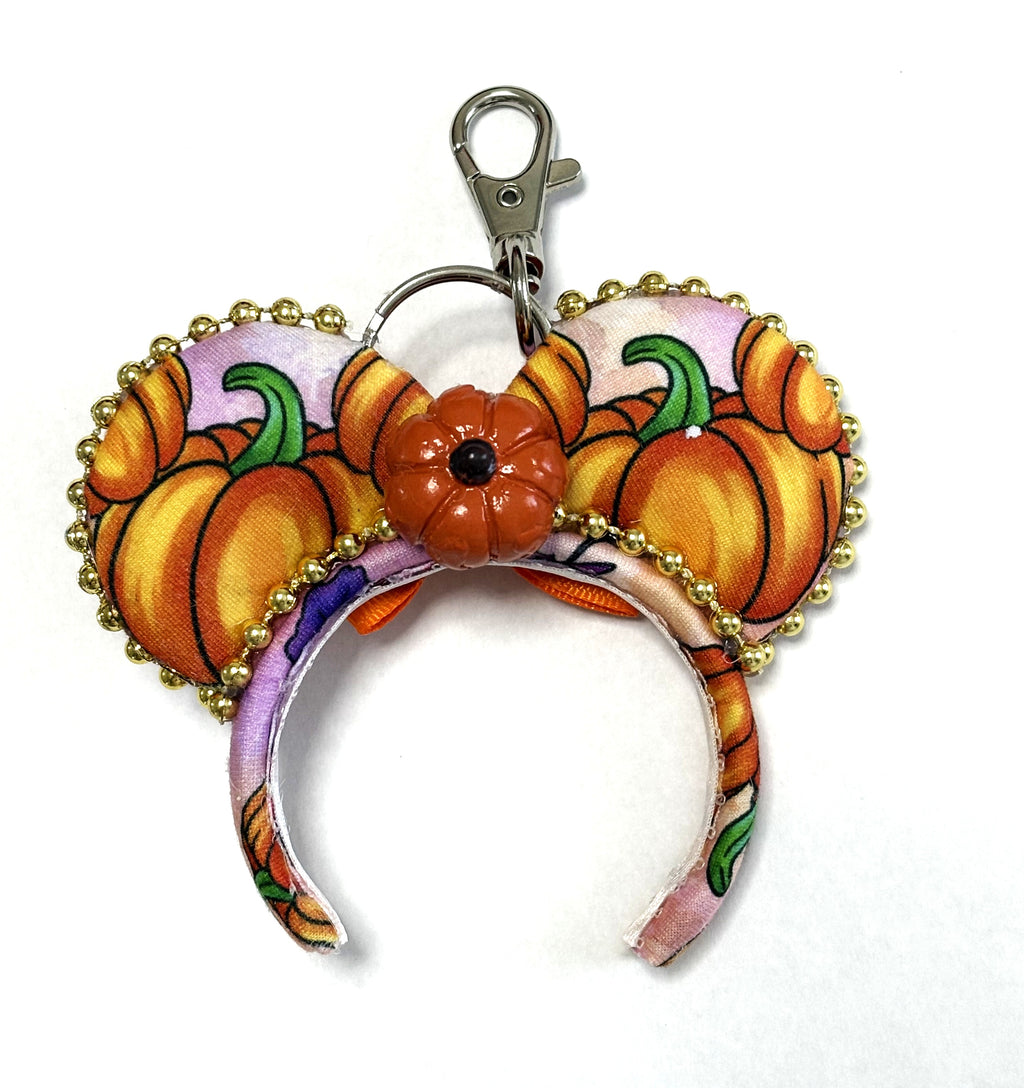 Handcrafted Pumpkin Patch Magic mini mouse ear keychain and bag charm featuring colorful autumn pumpkin-print fabric, sparkling gold beaded trim, and a decorative pumpkin centerpiece.