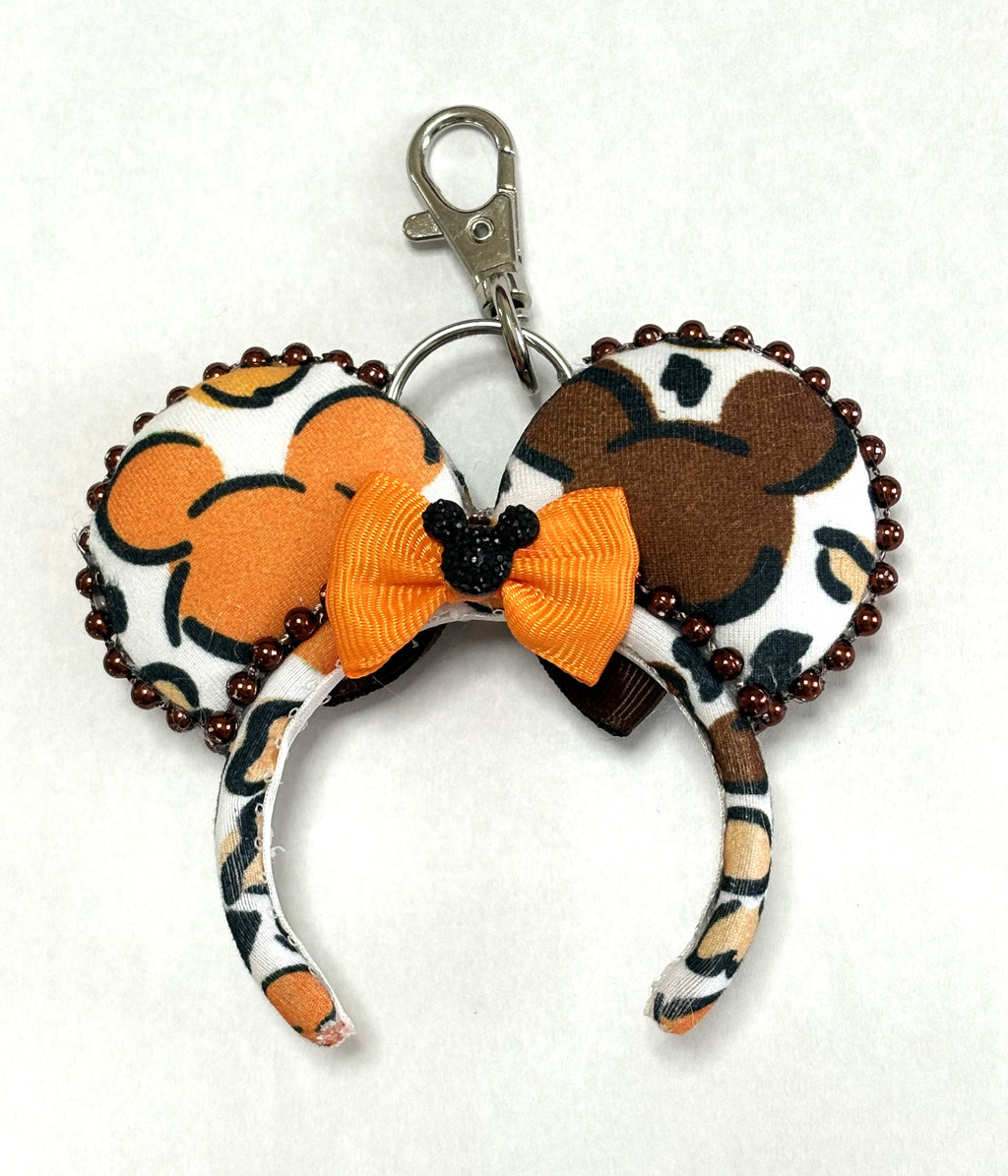 Handcrafted Harvest Mouse Magic mini ear keychain and bag charm featuring colorful autumn mouse silhouettes, copper-brown beaded trim, a golden-orange bow with a sparkling black centerpiece, and a metal clasp.