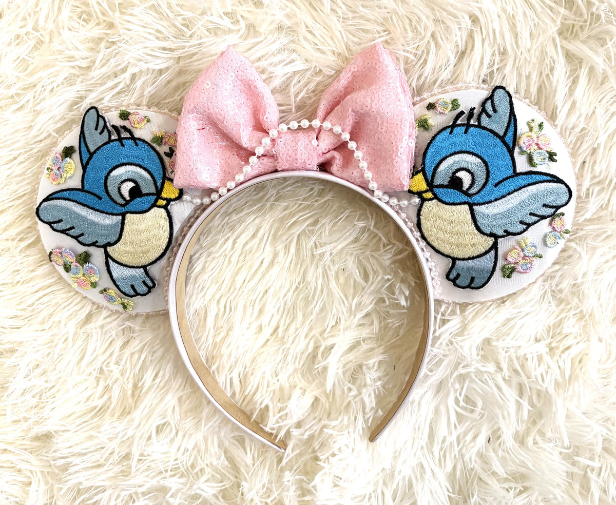 Handcrafted Enchanted Helpers mouse ear headband with embroidered blue songbirds, pastel floral details, pearl-beaded trim and soft pink sequin bow.