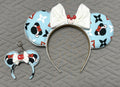 Frosted Holiday Magic Pixie Pair featuring a handcrafted icy blue Christmas mouse ear headband with pearl trim, oversized white bow, and matching mini ear bag charm with red mitten accent.