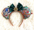 Christmas Wishes & Jingle Bells handcrafted mouse ear headband featuring festive Christmas character fabric, emerald-green velvet bow, gold glitter starburst, gold beaded trim, and colorful jingle bells.