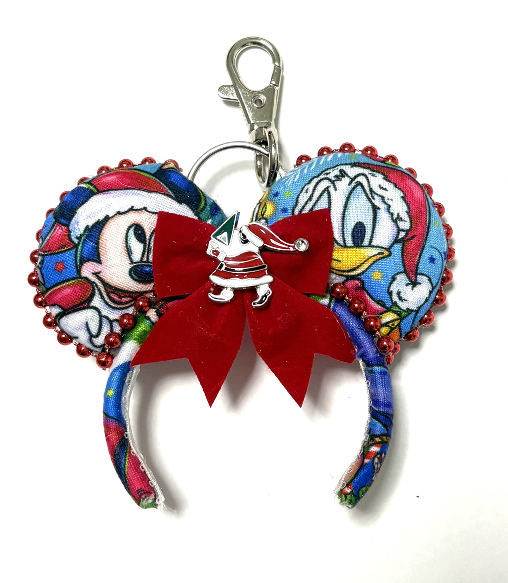 Merry Mouse & Mistletoe mini Christmas mouse ear keychain with festive character fabric, red velvet bow, silver holiday bell accent, red bead trim, and lobster clasp.