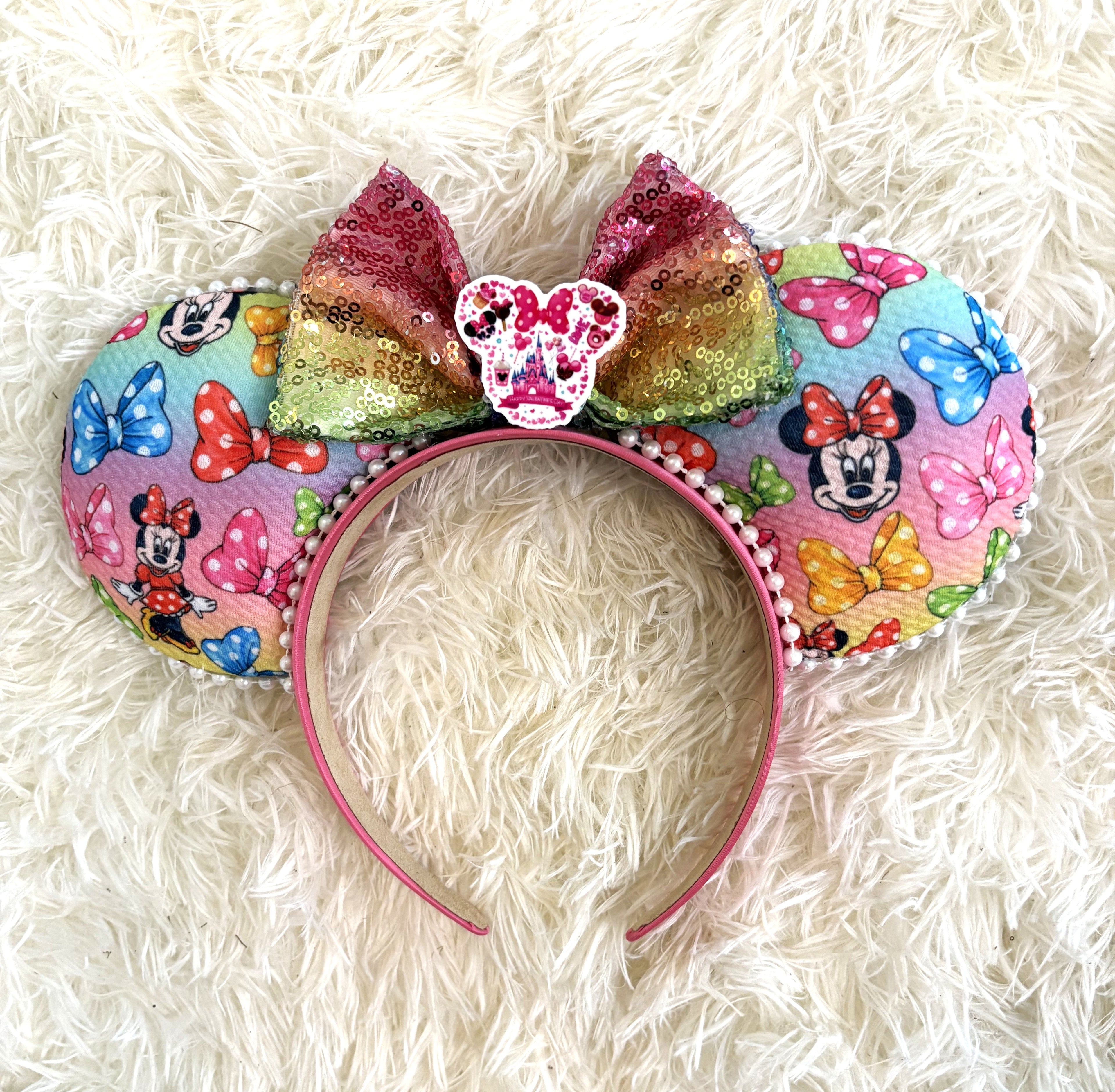 Handcrafted mouse ear headband featuring colorful bow-inspired artwork on pastel rainbow fabric with an ombré sequin bow and boutique handcrafted styling.